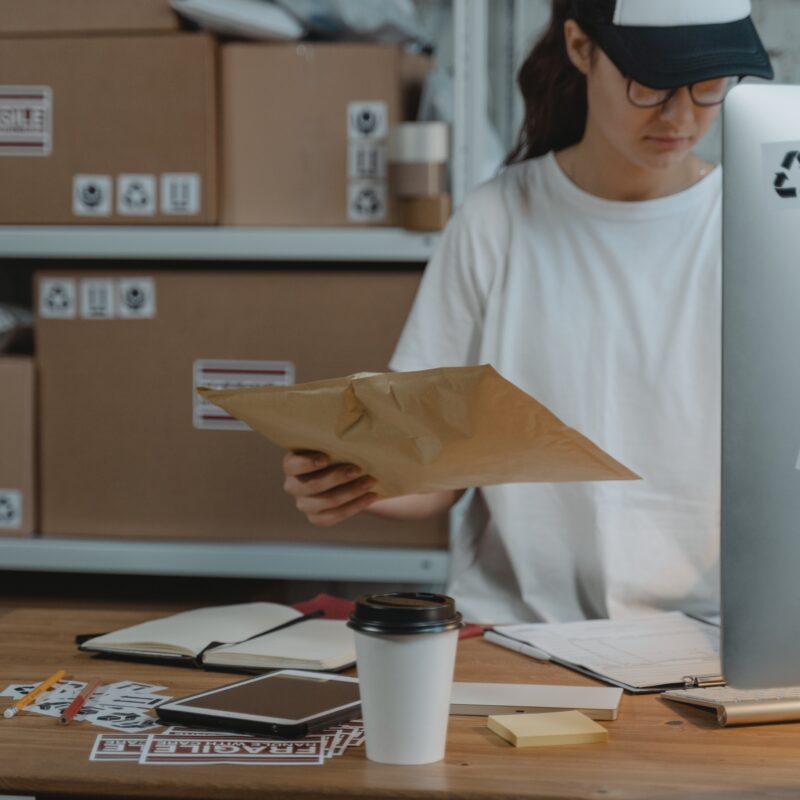 Woman is white clothing sorting mailroom items while standing at computer