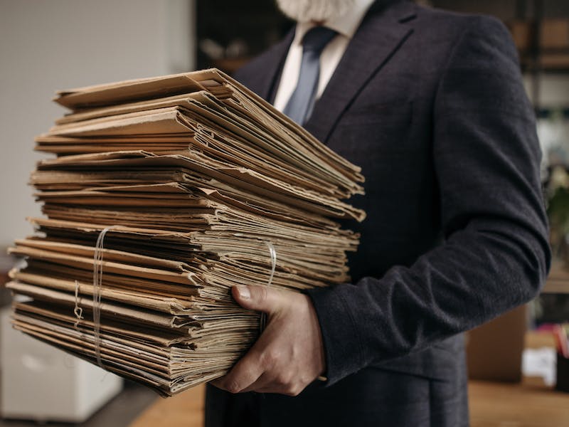 Man in suit holding a stack of brown files of paperwork